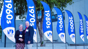 Gary Canner and his wife standing in front of flags with MDC class decade years