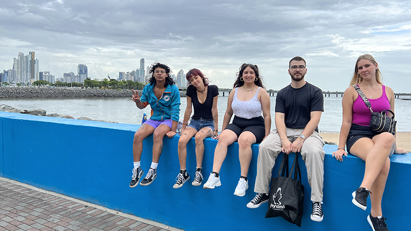 Five persons sitting on a wall by the water