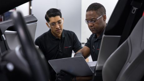 Two male students looking at a car and laptop