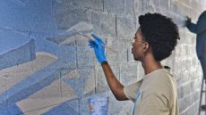 Student painting wall mural with blue paint.