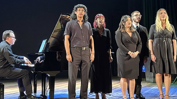 five students on stage singing accompanied by piano player