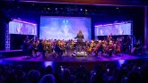 a conductor leading a live orchestra with animation on the screen