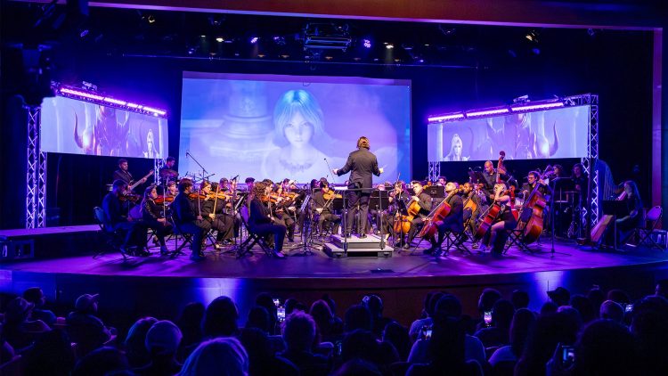 a conductor leading a live orchestra with animation on the screen