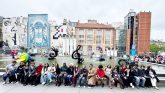 Group of students sitting in a line in front of buildings.
