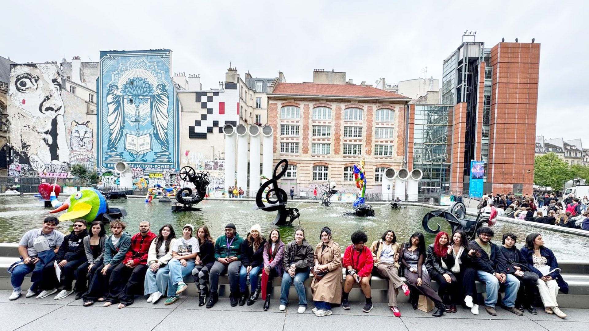 Group of students sitting in a line in front of buildings.