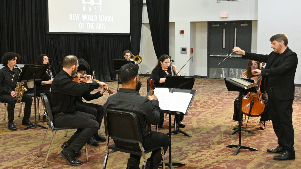 Eight people playing their instruments conducted by Dr. Grant Gilman.