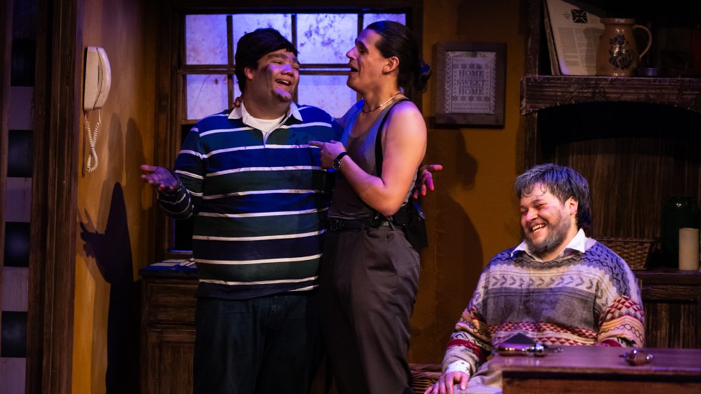 Three student actors smiling and acting on stage.