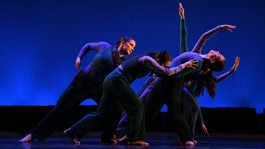 Four dancers dancing on stage dressed in blue.