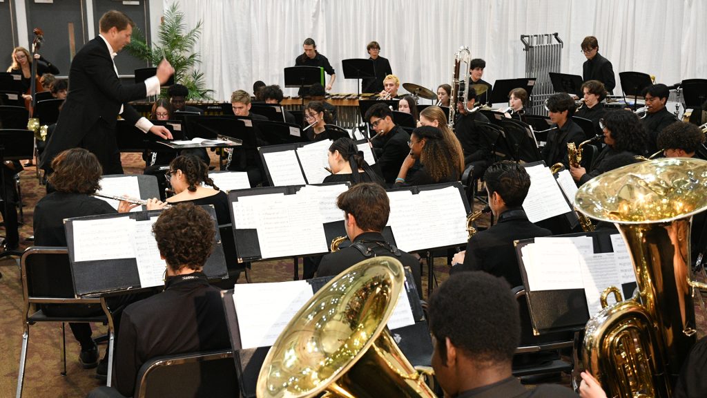 Brent Munger directing an orchestra of students playing wind instruments.