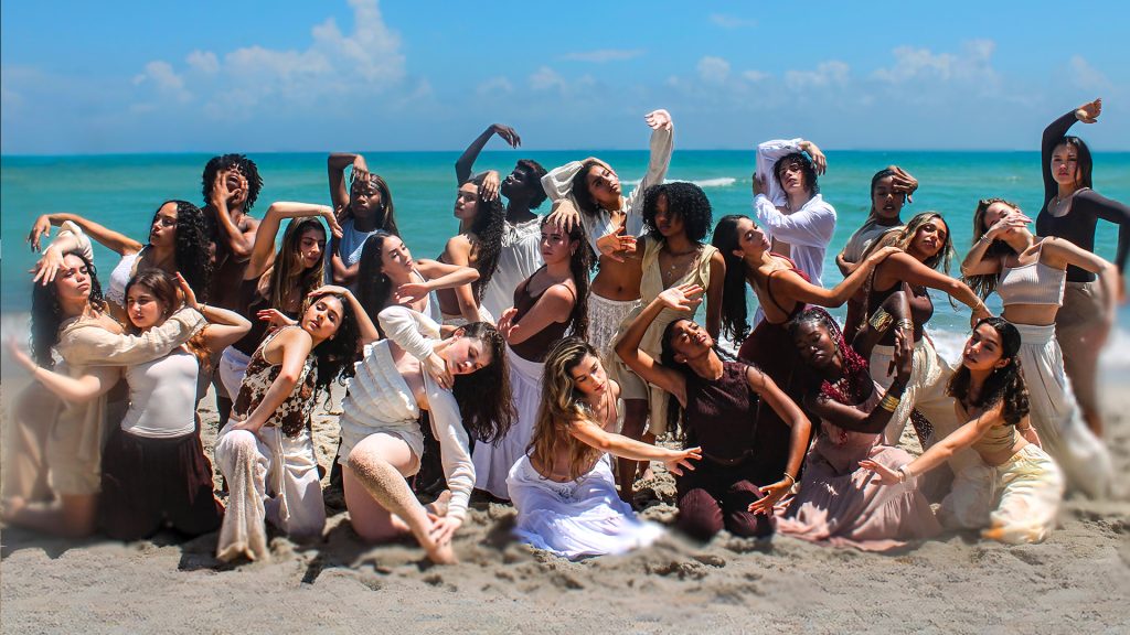 Large group of students posing on the sand by the beach.