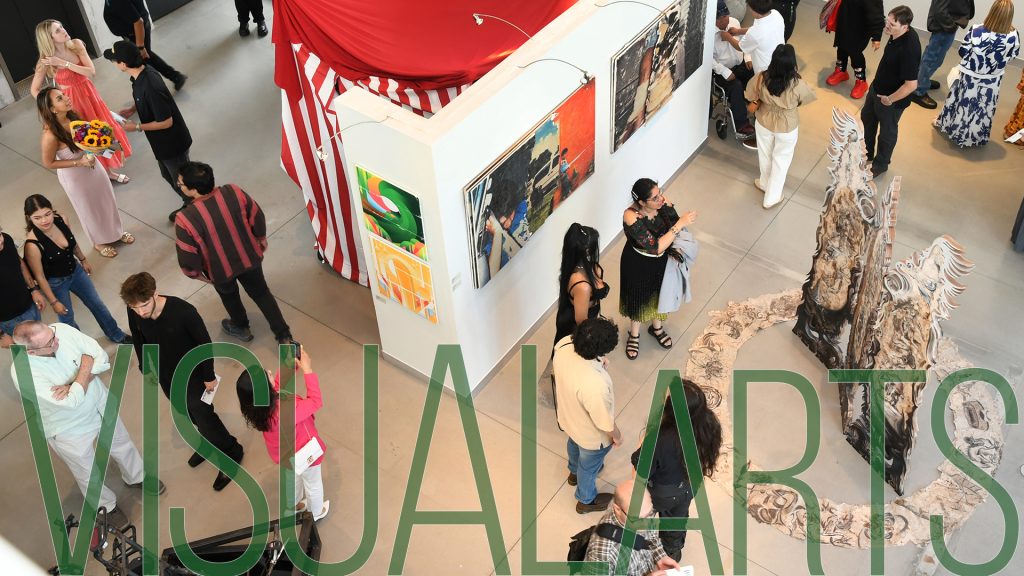 Birds-eye view of gallery with guests interacting around floor sculpture and wall with paintings.