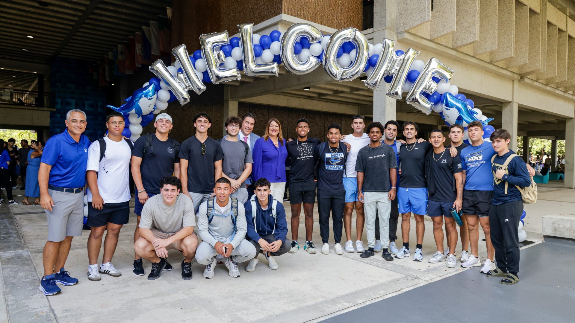 Students with the college president under an arch of balloons