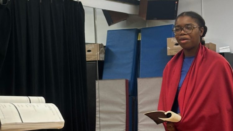Person with red cape holding a notebook.