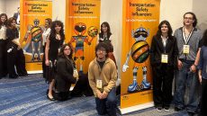 Group of people standing or sitting by three colorful upright banners.