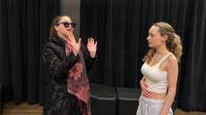 Two students acting in front of black curtain.