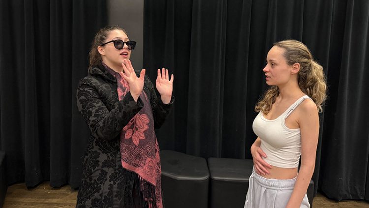 Two students acting in front of black curtain.
