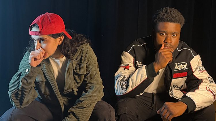Two people sitting pensively. One wearing a read cap.