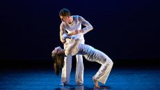 Two dancers on stage dancing dressed in white.