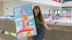 Girl in concrete building with various flags behind her holding a colorful poster.